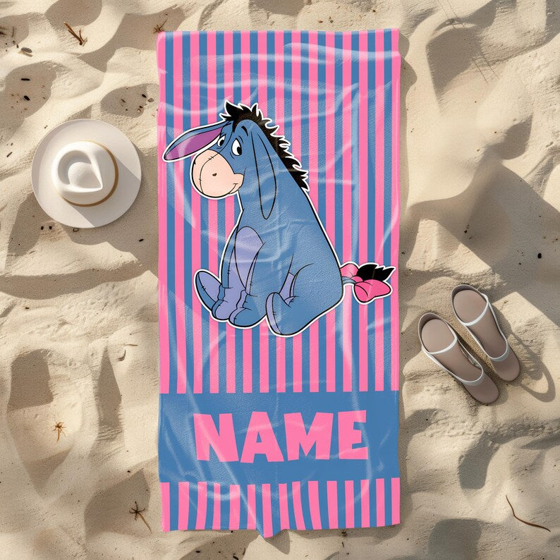 Custom blue and pink striped beach towel showcasing Eeyore from Winnie the Pooh sitting calmly, ideal for children or nostalgic adults, with space to add a name.