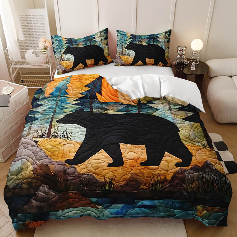 A quilted bedding set featuring a large black bear silhouette walking across a stylized forest landscape with blue, teal, orange, and brown tones, shown on a bed with matching pillowcases in a bedroom setting.