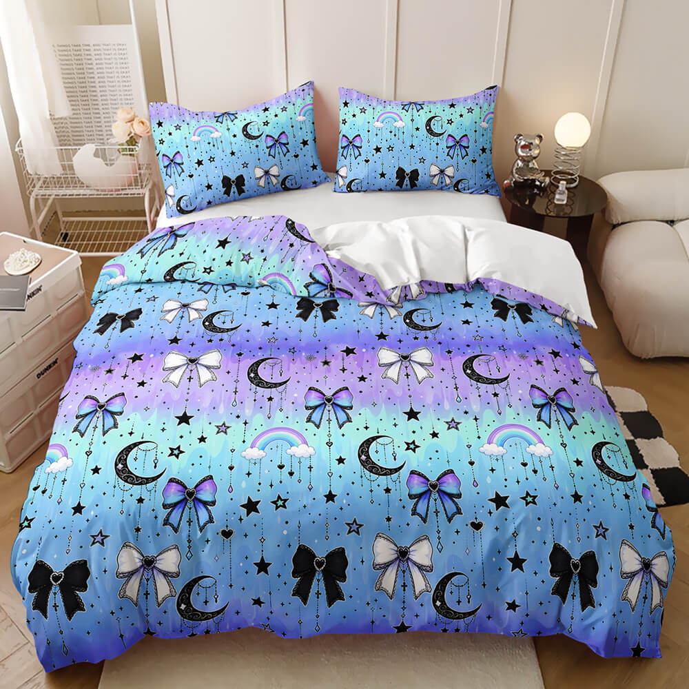 A bedding set displayed on a bed in a styled bedroom, featuring a duvet cover and two pillowcases with a colorful gradient pattern of blue, purple, and teal, decorated with black crescent moons, white bows, stars, and rainbows.