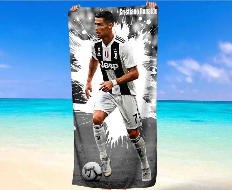 Cristiano Ronaldo towel laid out on the sand at the beach, perfect for sunbathing or drying off after a swim.