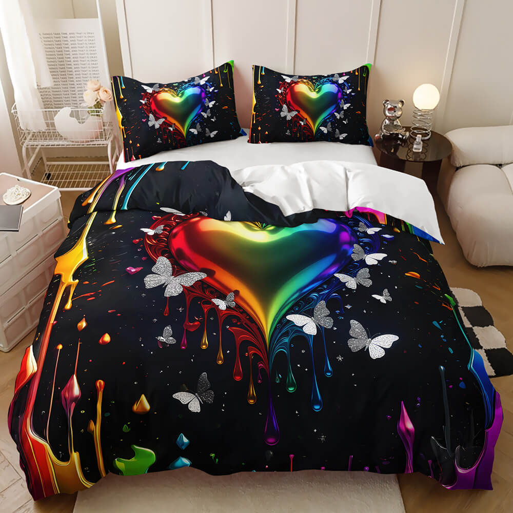 A bed dressed in a black bedding set featuring a large glossy rainbow heart with dripping paint effects and white butterfly prints, shown in a styled bedroom setting.