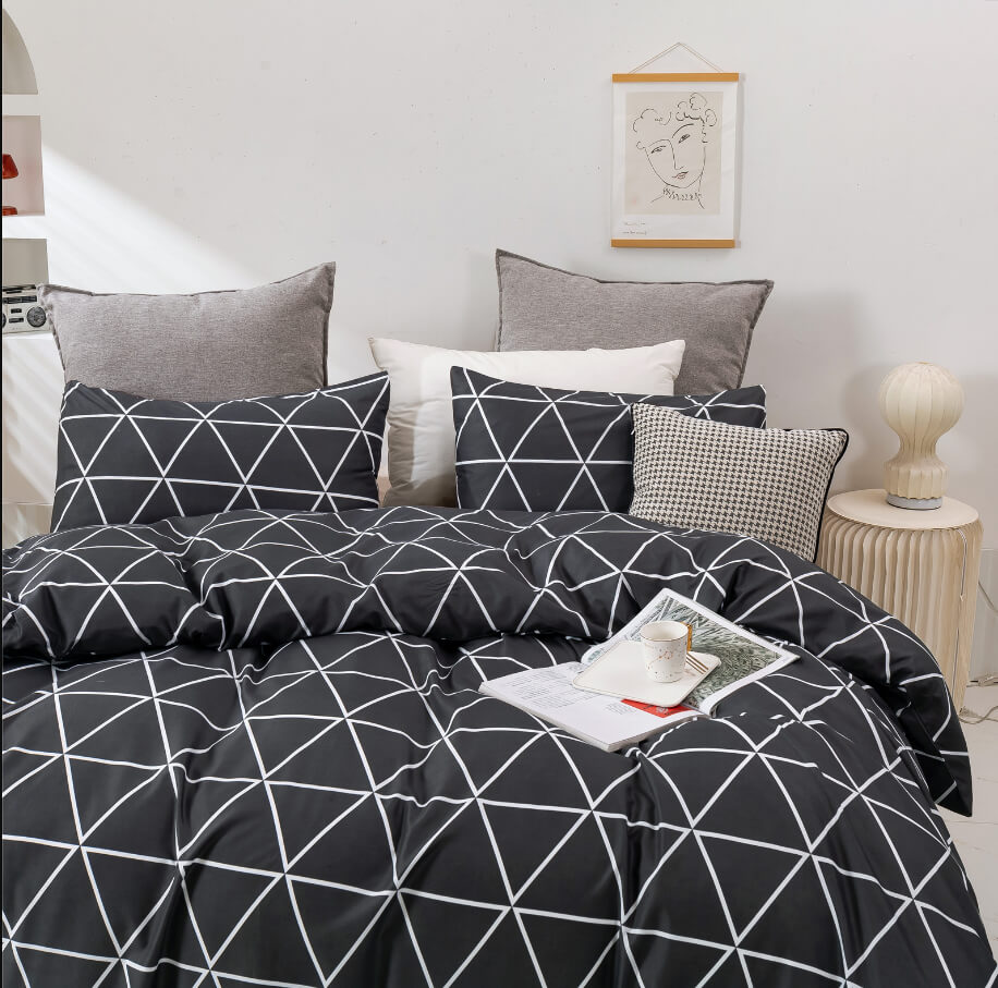 A bed dressed in a black bedding set with a white geometric line pattern, styled with gray and white pillows in a bright bedroom setting.