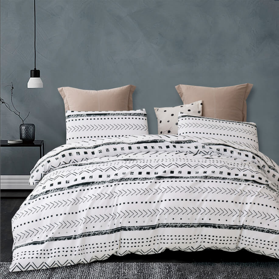 A bed dressed in a white bedding set with black geometric tribal-style patterns, modern styled