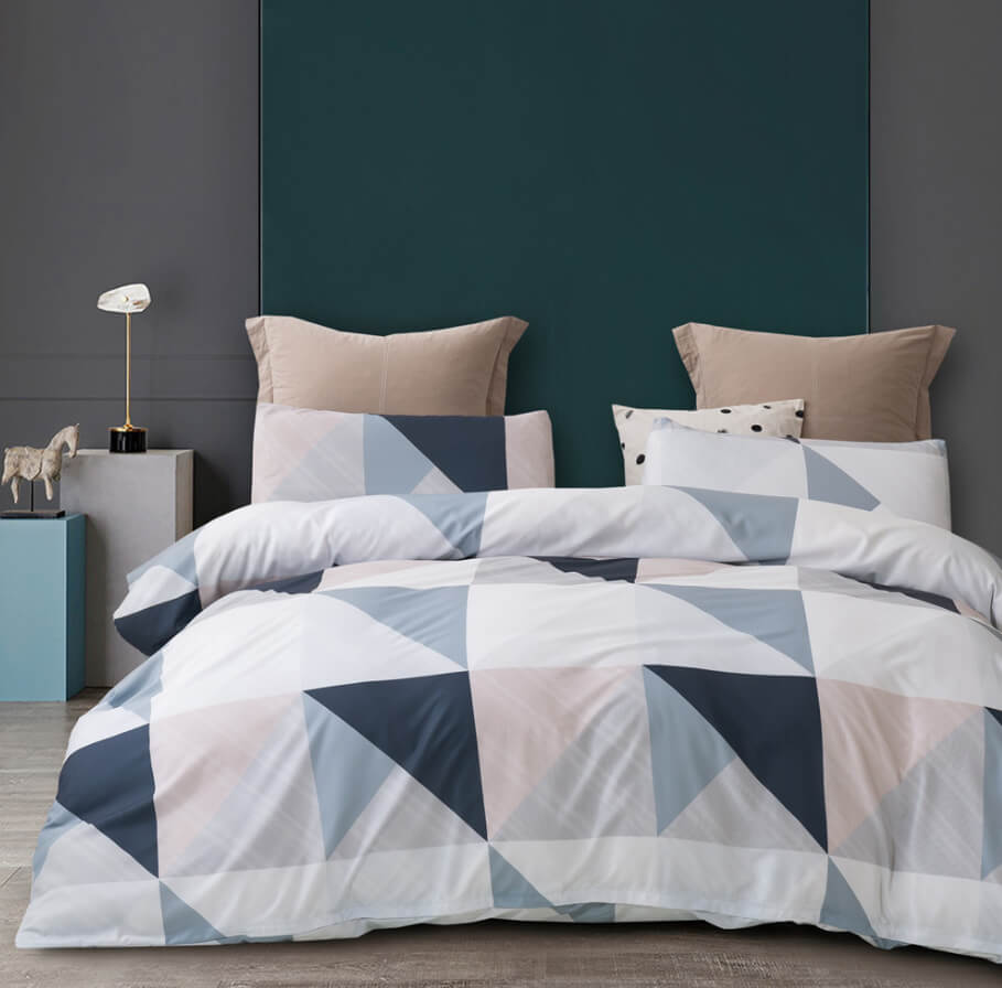 A bed dressed in a geometric patterned duvet cover and pillow shams, styled in a modern bedroom